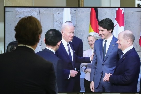 2022年3月24日，在比利時(shí)布魯塞爾的北約總部，一名男子觀看屏幕上美國(guó)總統(tǒng)拜登（右四）、歐盟委員會(huì)主席馮德萊恩（右三）、加拿大總理特魯多（右二）、德國(guó)總理朔爾茨（右一）出席七國(guó)集團(tuán)峰會(huì)合影儀式的畫面。新華社記者鄭煥松攝