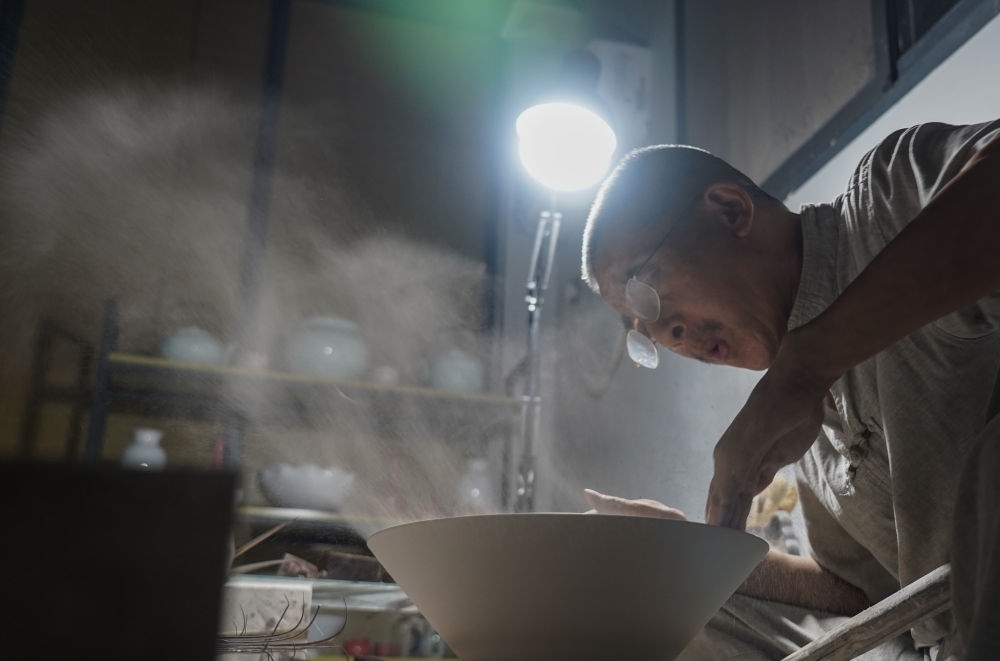 ↑ 在景德鎮(zhèn)，手工匠人吹去坯內(nèi)的泥土（2021年7月14日攝）。