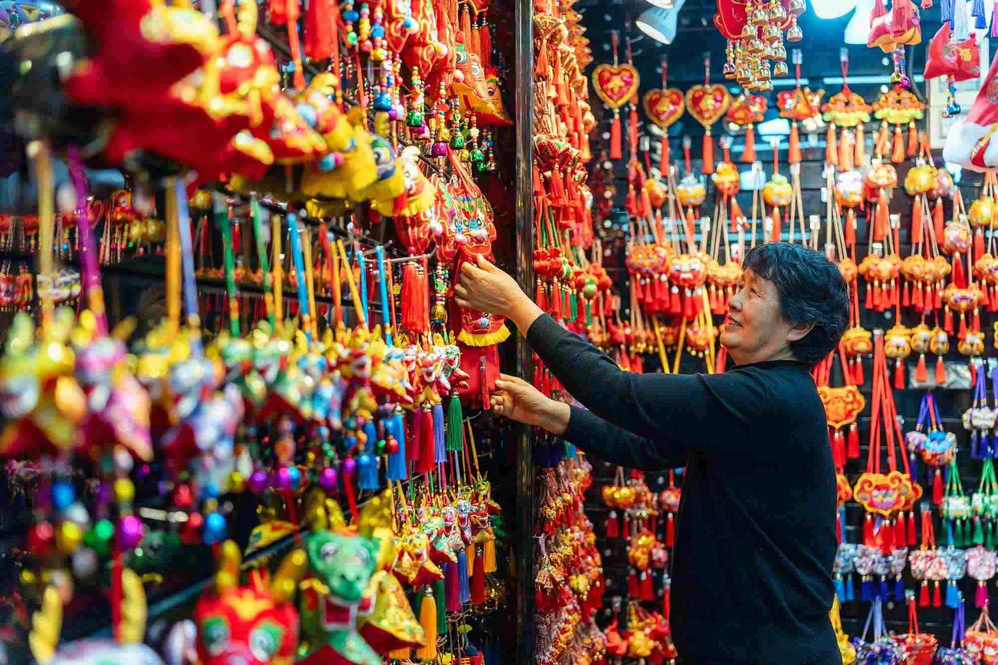 2023年12月11日，金華義烏國際商貿(mào)城，龍年喜慶用品掛滿攤位，顧客正在挑選中。