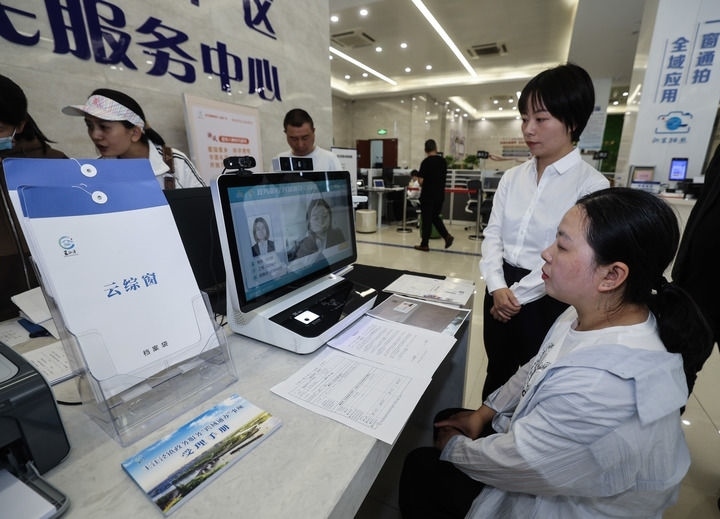在浙江省嘉興市秀洲區(qū)王江涇鎮(zhèn)便民服務(wù)中心的“跨域通辦·云綜窗”窗口，辦理開(kāi)業(yè)登記的個(gè)體工商戶（右一）通過(guò)該系統(tǒng)與江蘇省蘇州市吳江區(qū)盛澤鎮(zhèn)行政審批局工作人員視頻連線，進(jìn)行身份讀取及材料線上審核（2024年5月9日攝）。新華社記者 徐昱 攝
