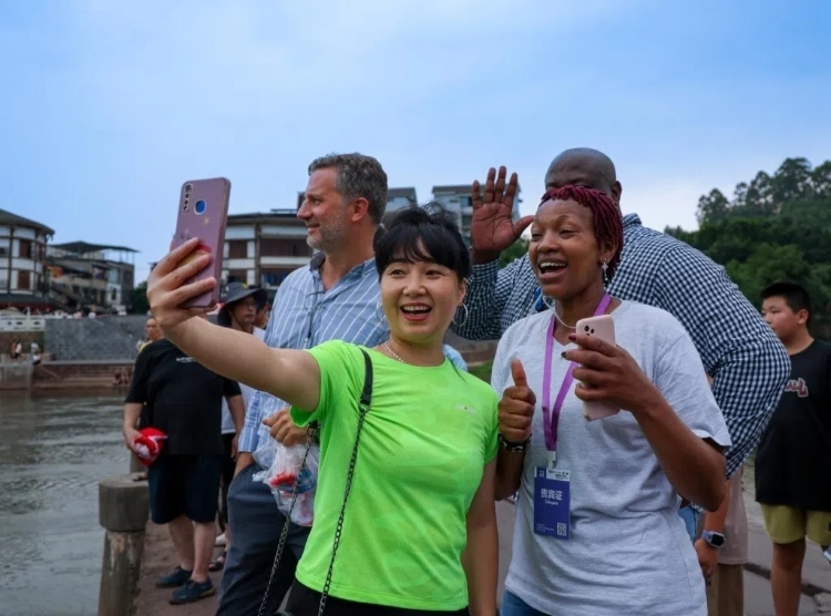 2024“一帶一路”媒體合作論壇聯(lián)合采訪調(diào)研行成員在樂山蘇稽古鎮(zhèn)與游客合影留念。本報記者 伊霄攝