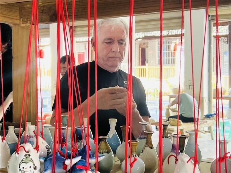 鄉(xiāng)愁如同一根根紅線，將游子與故鄉(xiāng)永遠(yuǎn)地牽連到一起。花茂村陶藝文化創(chuàng)意一條街的母氏陶藝館內(nèi)，紅線吊著陶瓶，思緒游走萬里。摩爾多瓦“信息標(biāo)簽”通訊社社長亞歷山大·塔納斯端詳著館內(nèi)展示的陶藝作品，并挑選出心儀的小擺件帶回摩爾多瓦，也帶走花茂村的“鄉(xiāng)愁”。（張亞欣攝）