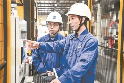 在廣西柳工機械股份有限公司生產(chǎn)車間內，一名高級技師（右）給徒弟講解數(shù)控設備操作細節(jié)。新華社記者 曹祎銘攝