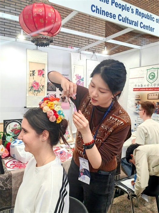 展覽正值羅馬尼亞迎春花節(jié)，國(guó)際中文教師志愿者潘婧穎向游客們介紹了國(guó)家非物質(zhì)文化遺產(chǎn)——福建泉州的簪花文化。布加勒斯特大學(xué)孔子學(xué)院供圖。